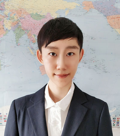 Mengtian Chen stands in front of a world map and looks into the camera