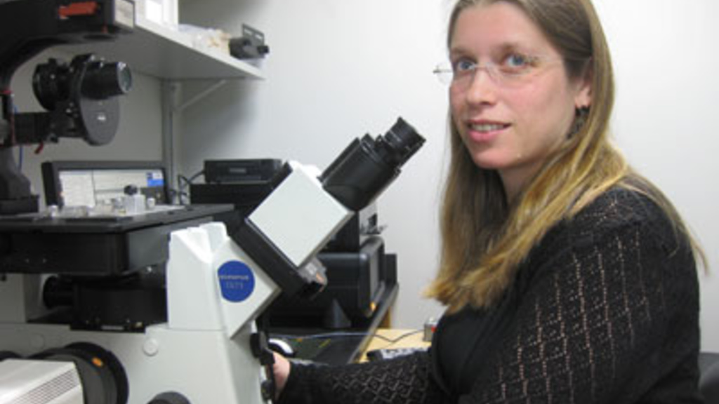 Sarit Smolikove sits at a microscope and looks into the camera
